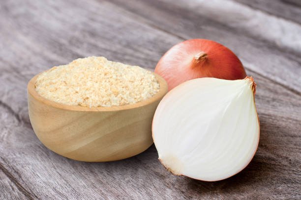 Ground onion or onion powder in wooden bowl and fresh onion with half sliced isolated on wooden table background.